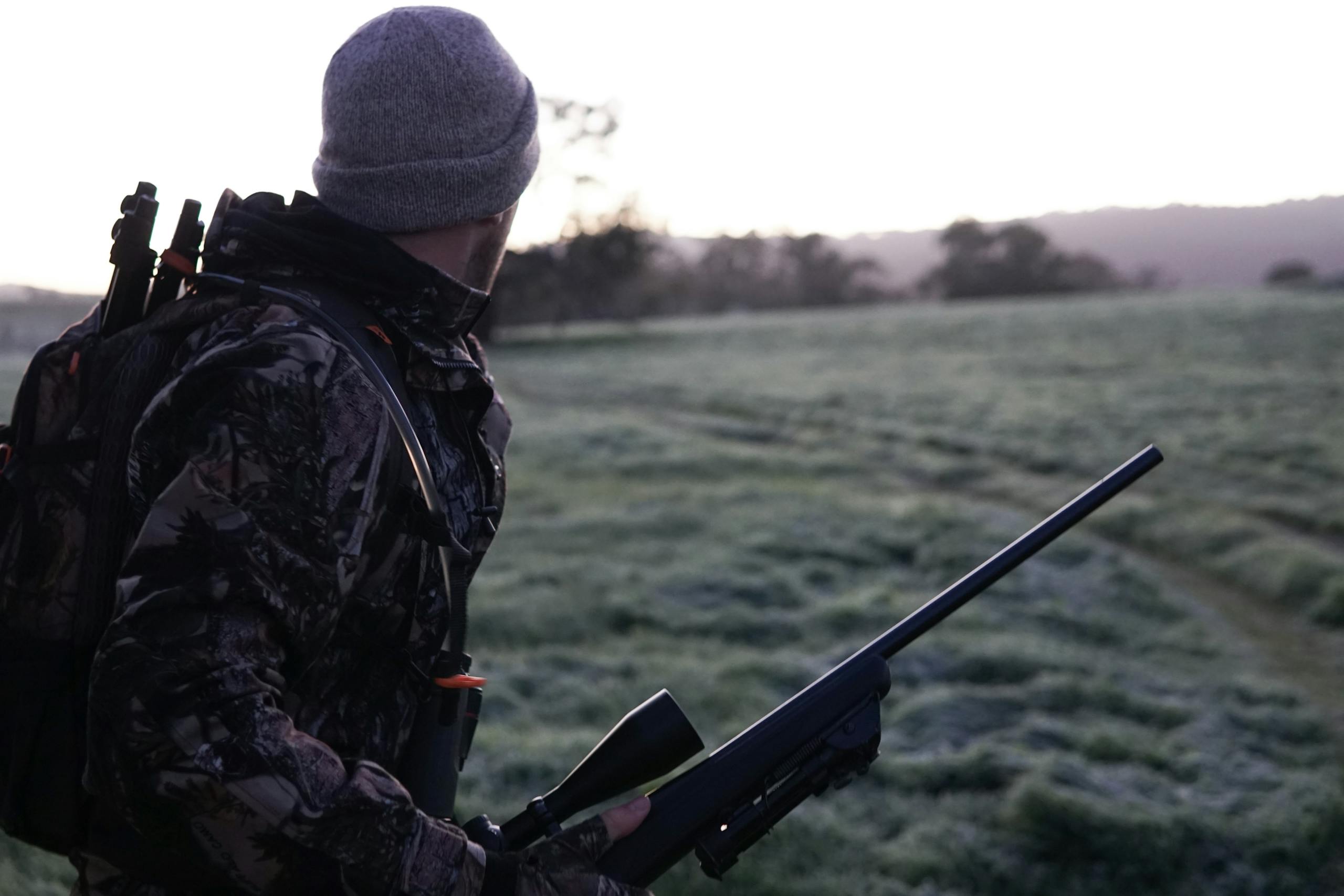 Camouflaged hunter surveying the landscape with rifle at dawn in Victoria, Australia.